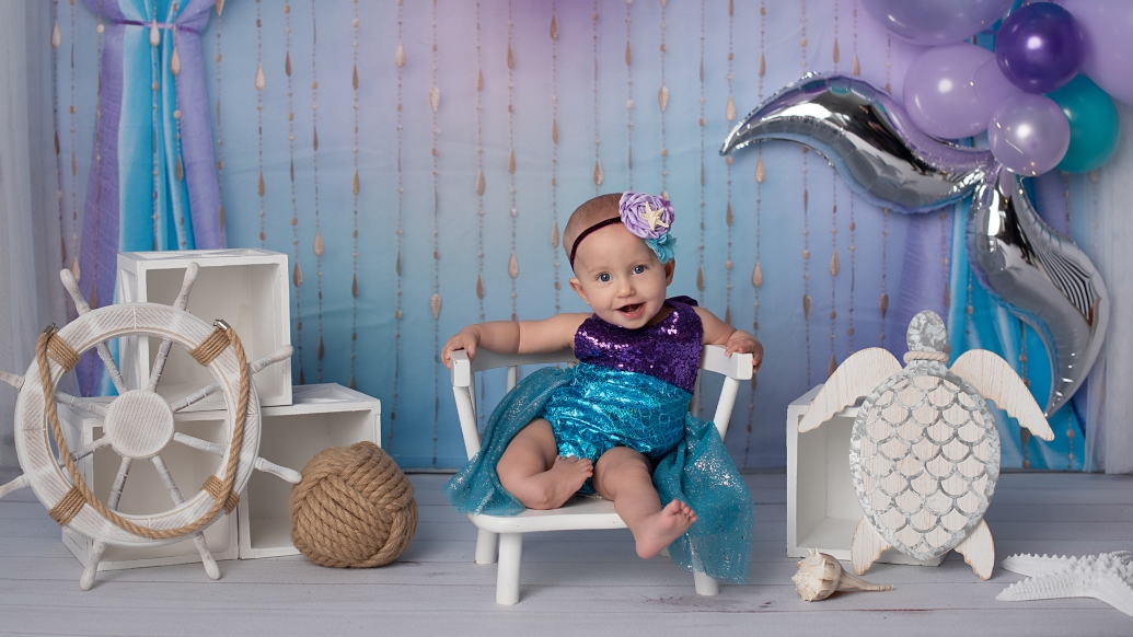 Baby sitting on chair smiling with purple background and props