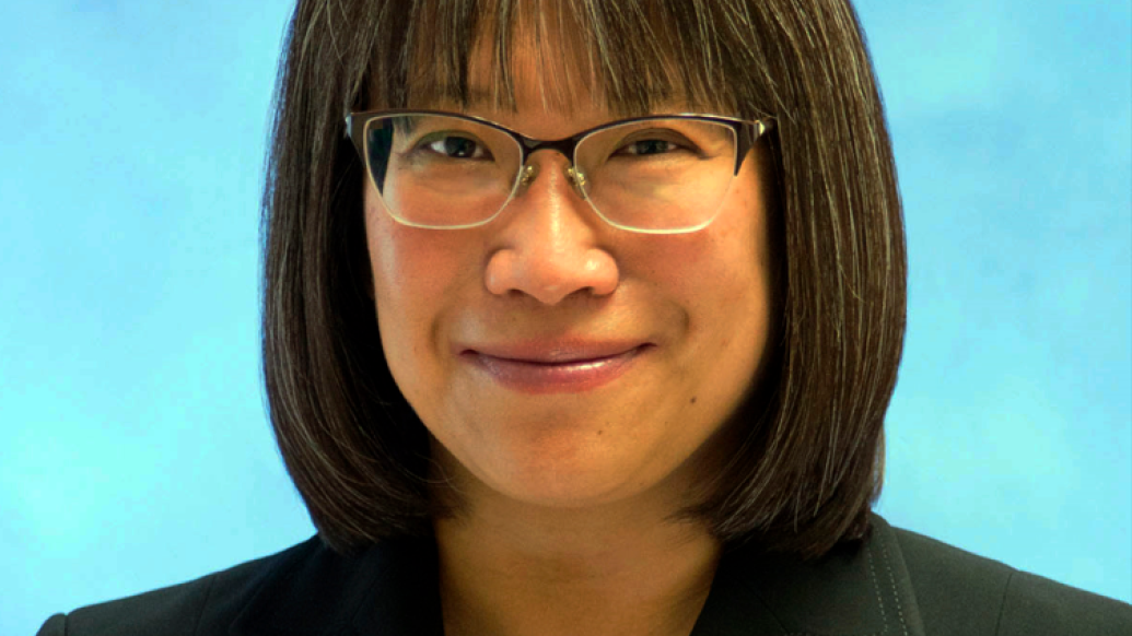 Professional portrait of a middle aged Asian woman who has shoulder-length black hair and is wearing glasses and a black blazer