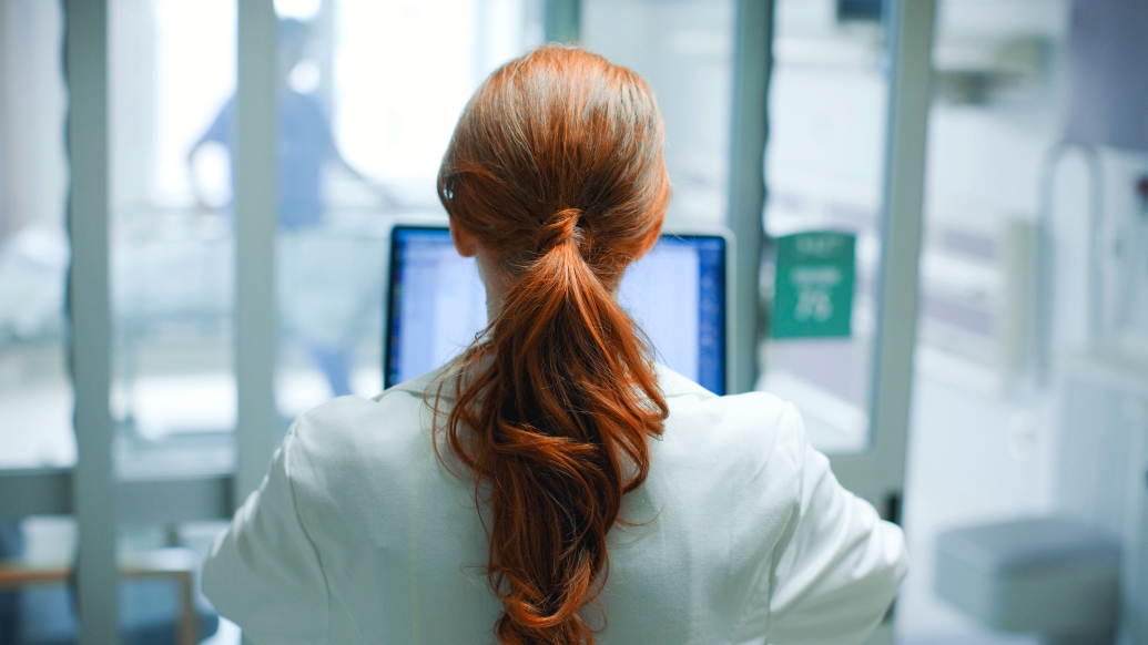 red hair woman looking at screen of computer in white coat