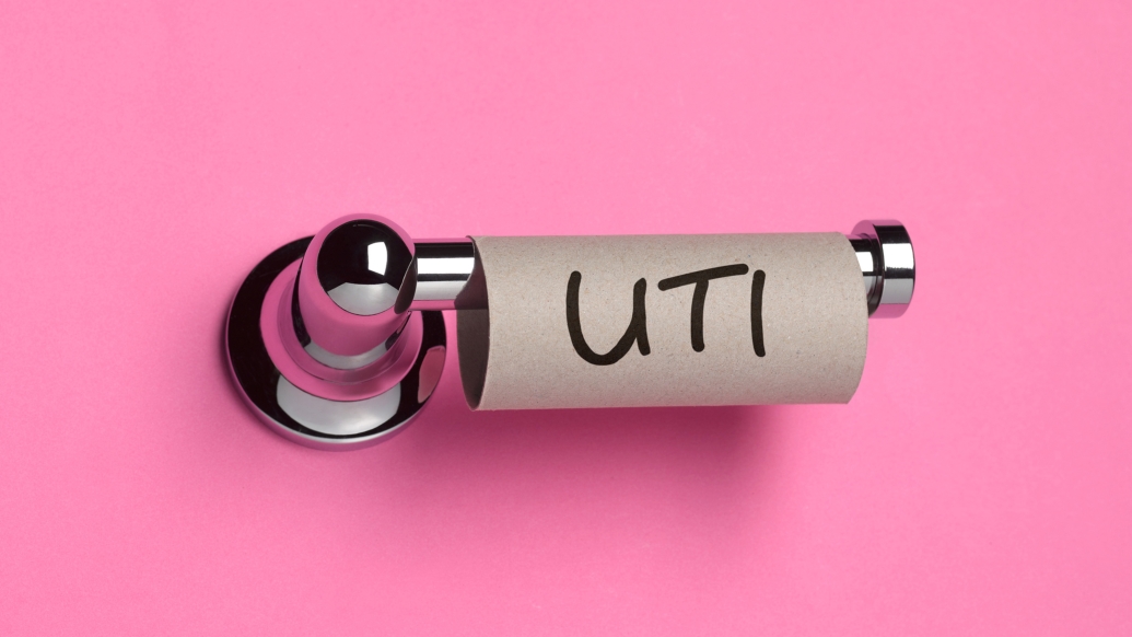 uti written on empty roll of toliet paper on a toliet paper holder with hot pink background