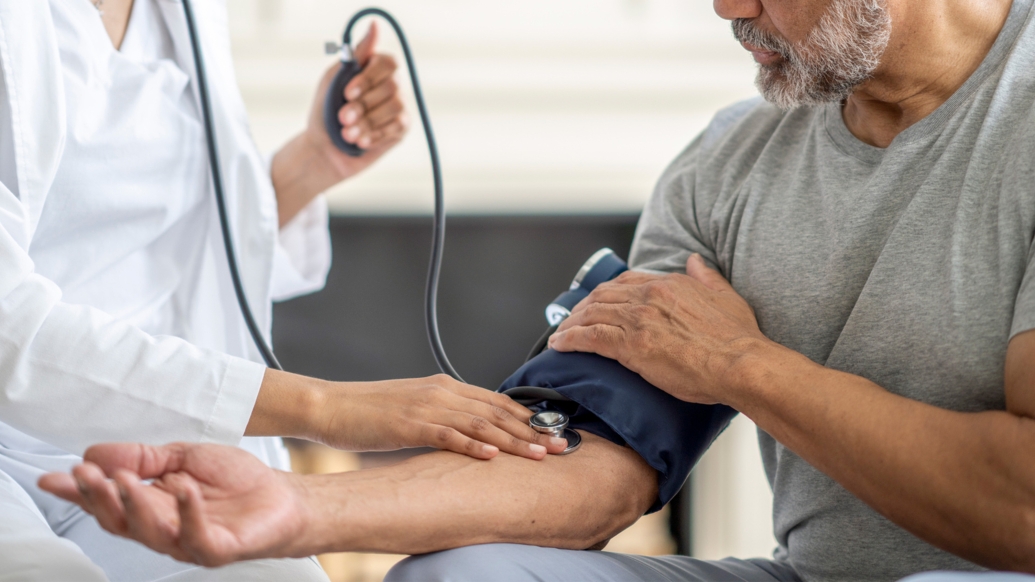 blood pressure cuff on mans arm with white coat doctor taking it 