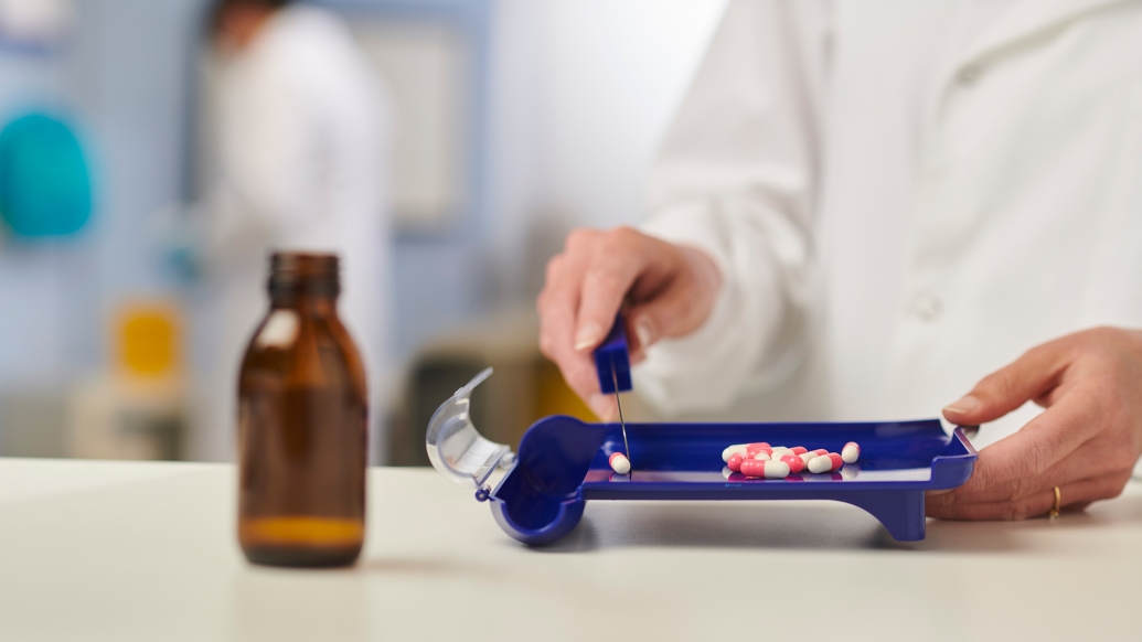 person at counter with medicine brown bottle and pills