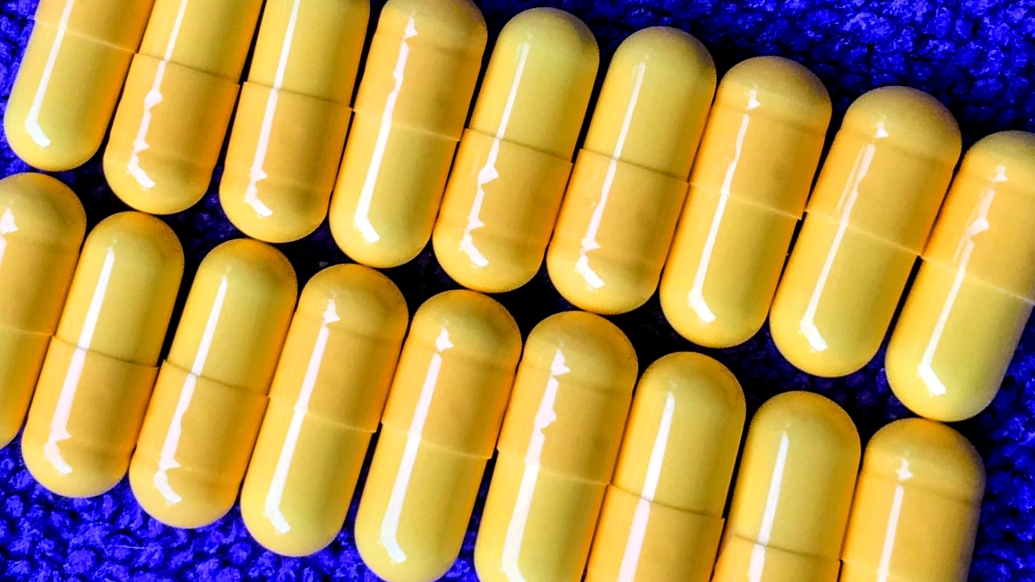 close up photo of yellow pills lined up on a bright blue matt