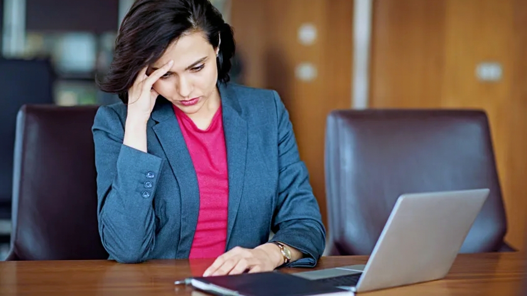 women looking stressed at desk in business suit and laptop and brown conference desk and leather brown chair