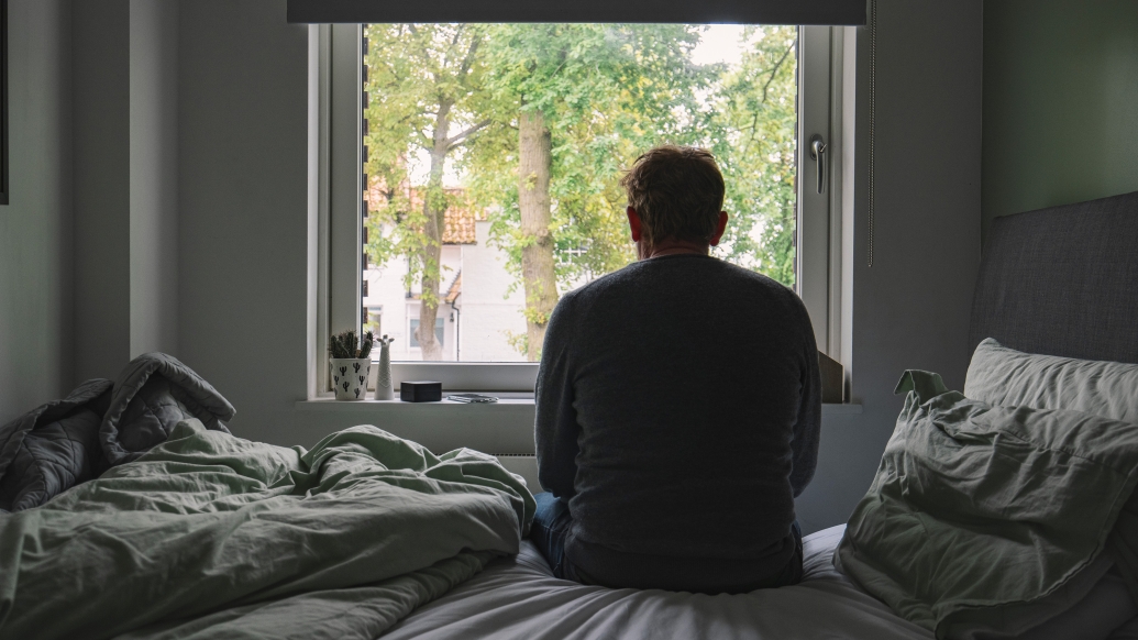 Man looking out window of bedroom. 