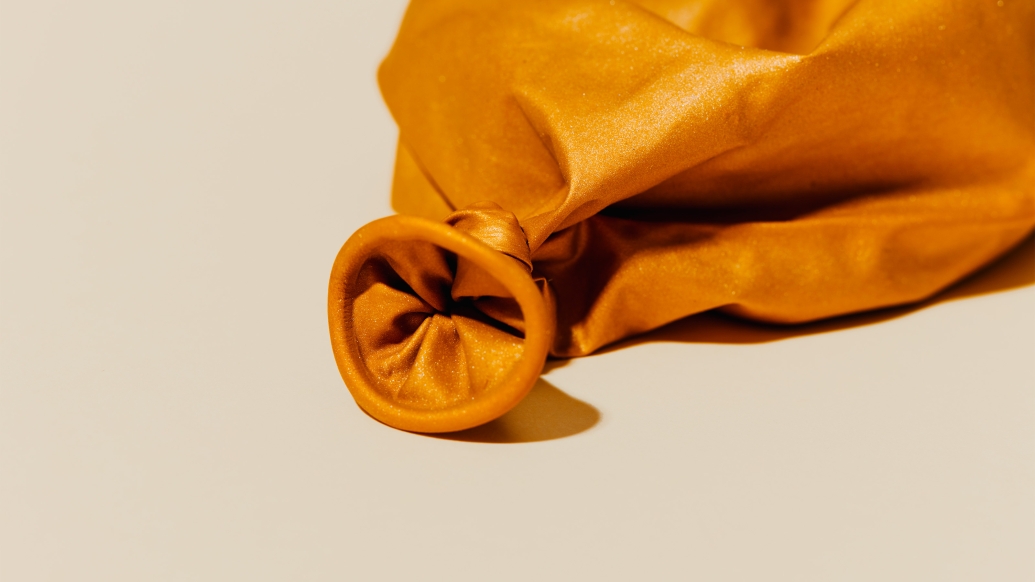 deflated orange balloon on white background close up on the part that's blown into