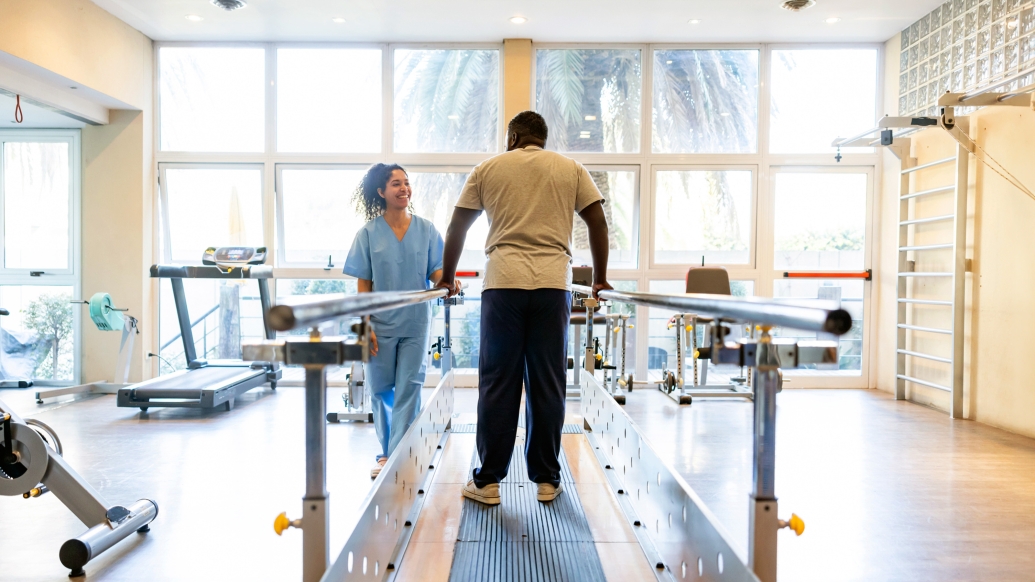 man walking on treadmill in open space with person in blue scrubs and scrub hat