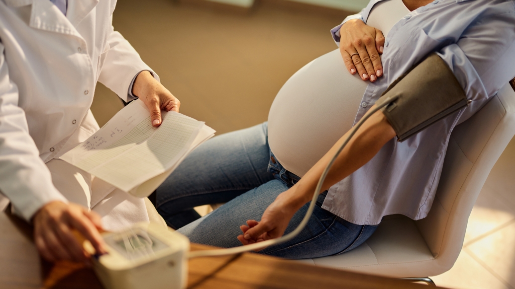 woman pregnant laying back with doctor looking at paper work and her getting blood pressure measured