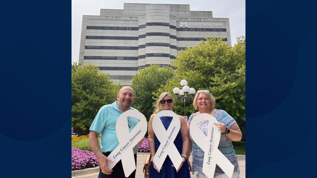 three friends standing outside rogel cancer center building with big white ribbons