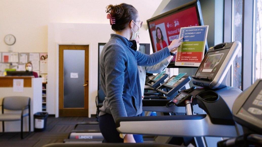 woman walking on treadmill picking intensity on a chart that reads from easier to harder