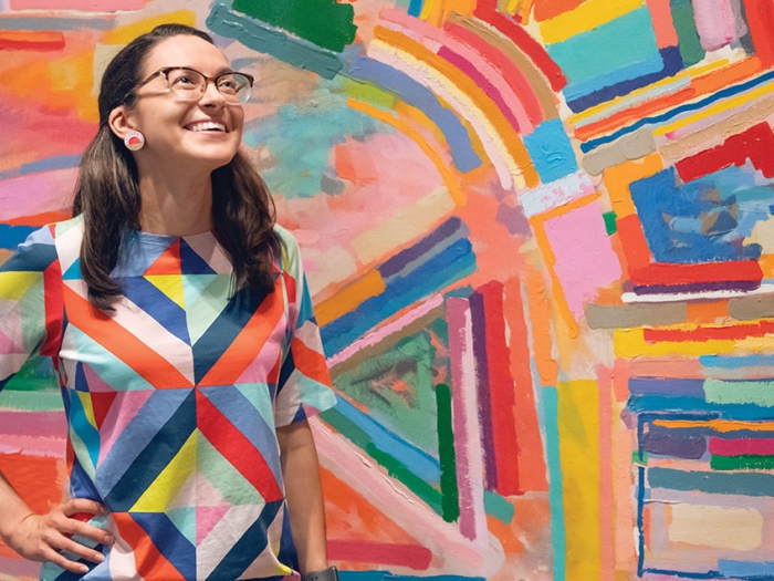 Emma smiles while standing in front of a colorful work of abstract art