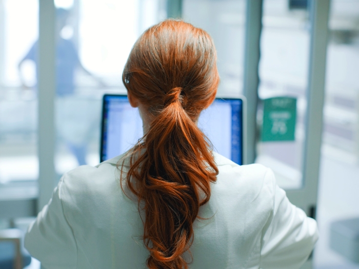 red hair woman looking at screen of computer in white coat