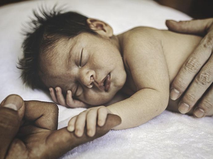 Sleeping baby hanging onto an adult's finger.