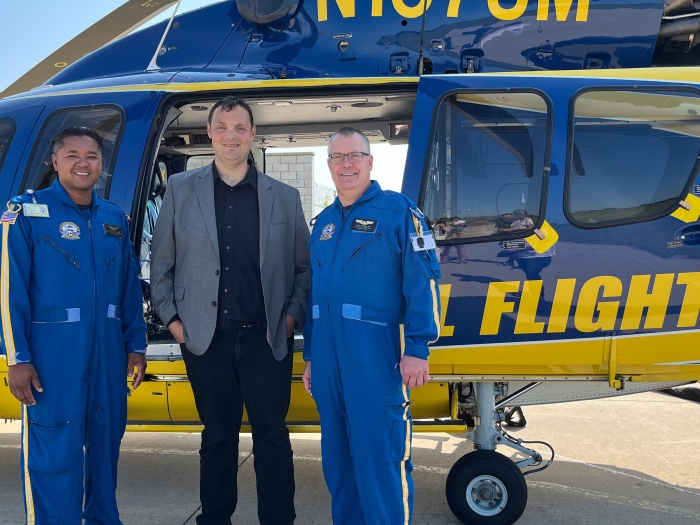 Survival flight pilots and person standing by helicopter smiling