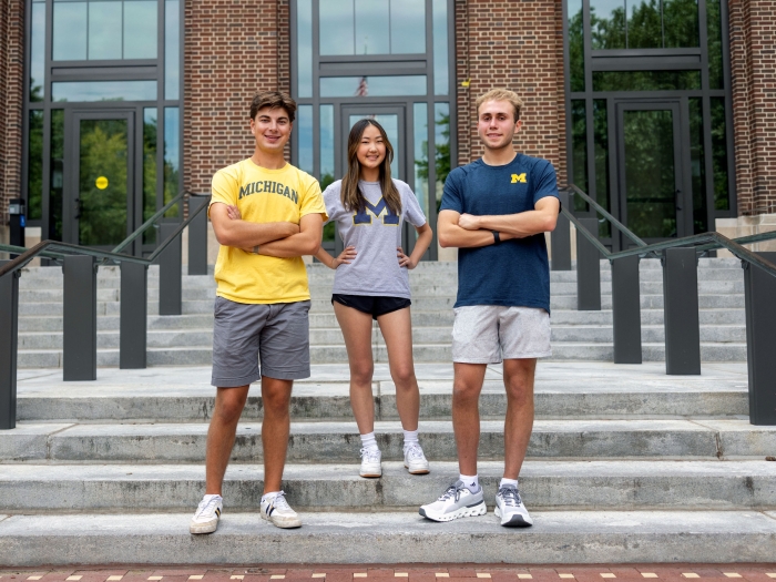 three students standing on stairs in Michigan shirts