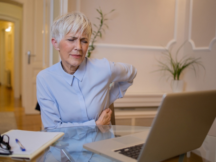 woman touching back leaning forward in pain at desk light powder blue button down