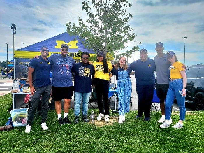 Group of people posing in front of a tree and tailgate tent