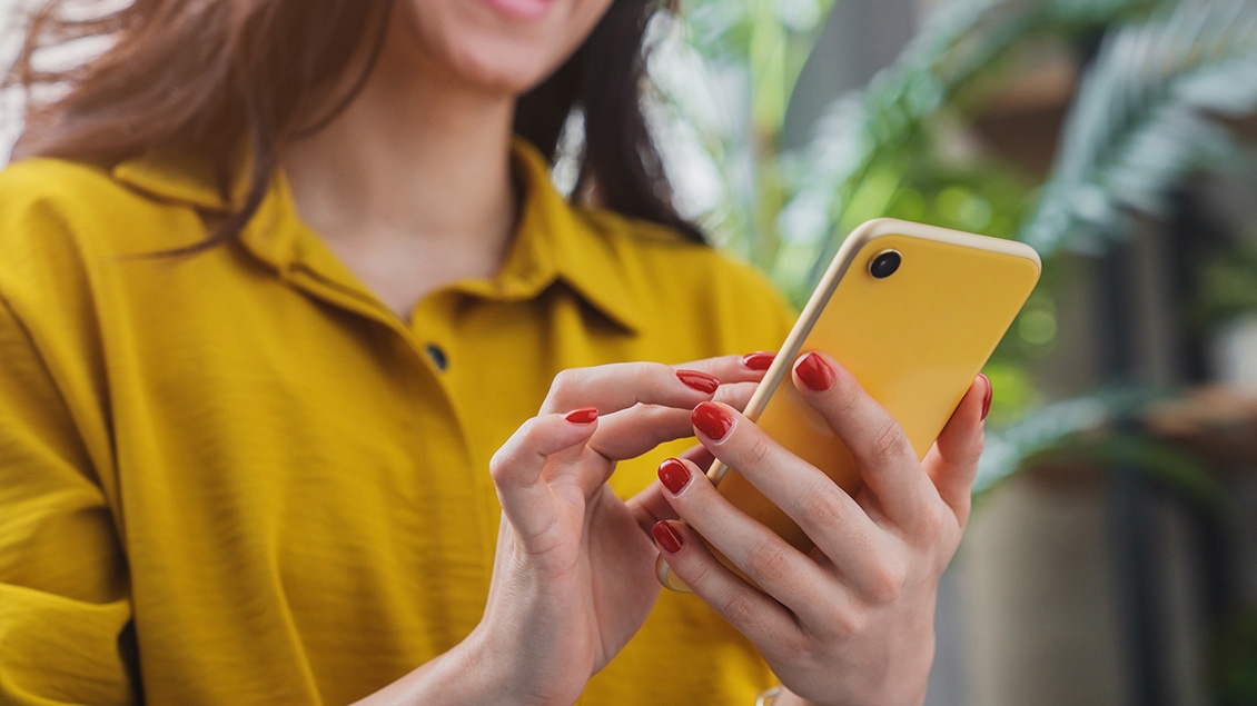 woman with red nail polish wearing a gold shirt holding an mobile phone