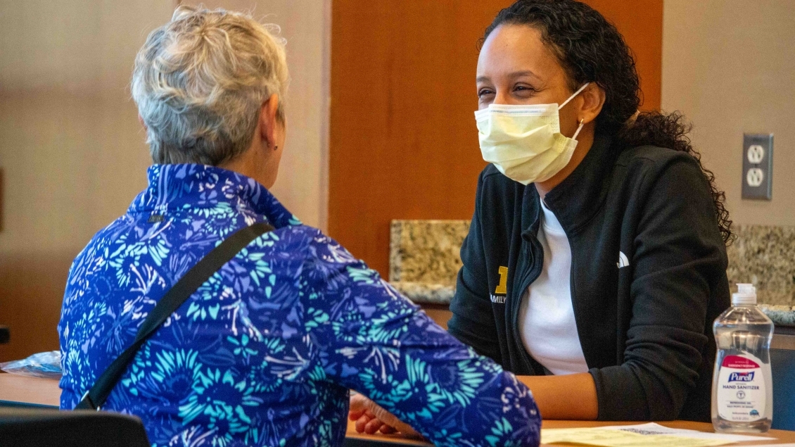 Masked woman helps patient check in at table