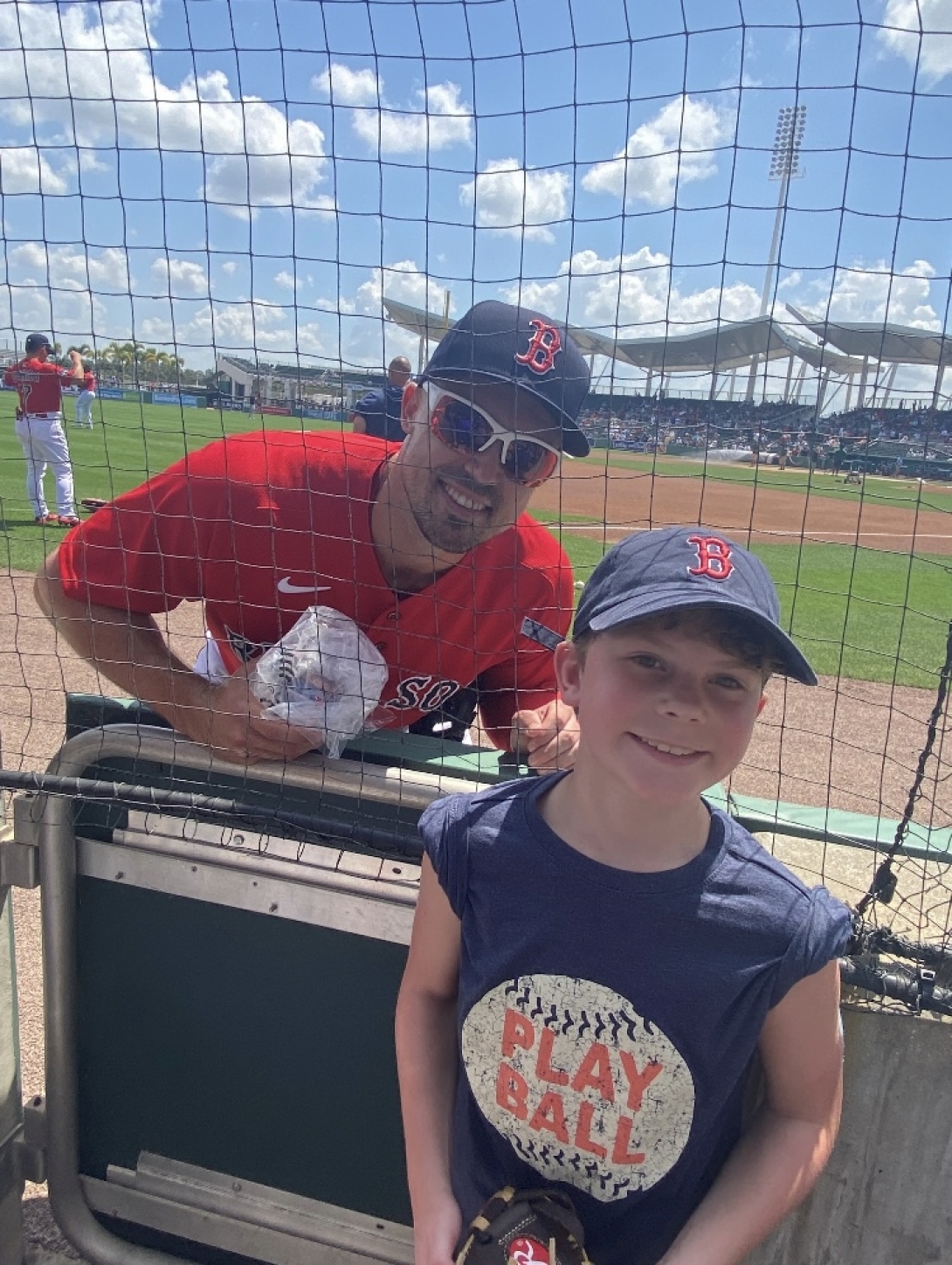 boston red sox player with boy in red sox hat smiling outside at baseball field