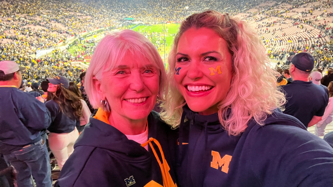 mom and daughter (right) wearing Michigan gear at a football stadium game smiling