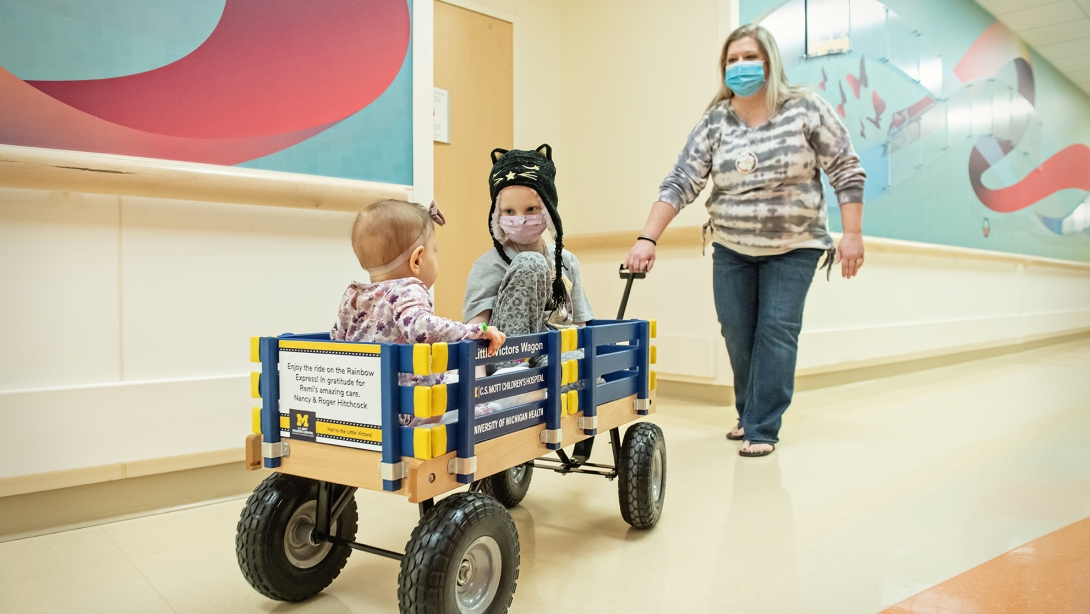 A hospital voluteer pulling two children in a wagon down a hospital hallway.