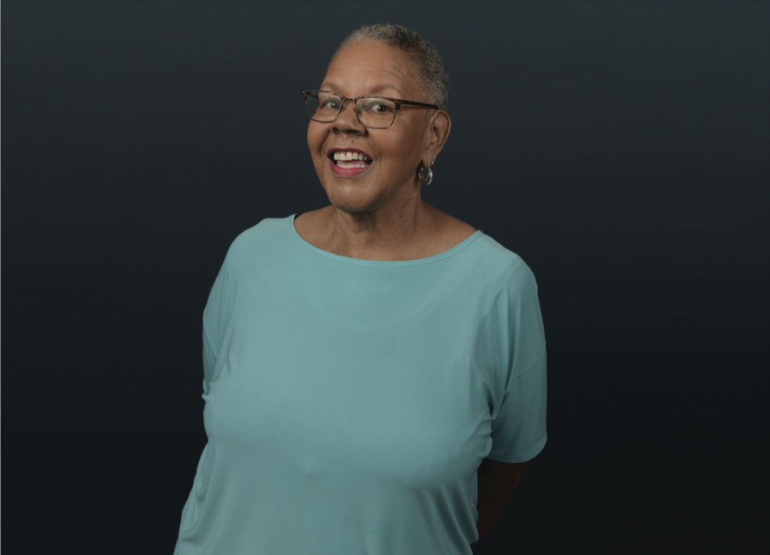 Portrait of Ann Chatman. She has short salt and pepper hair and is wearing glasses and a teal t-shirt.