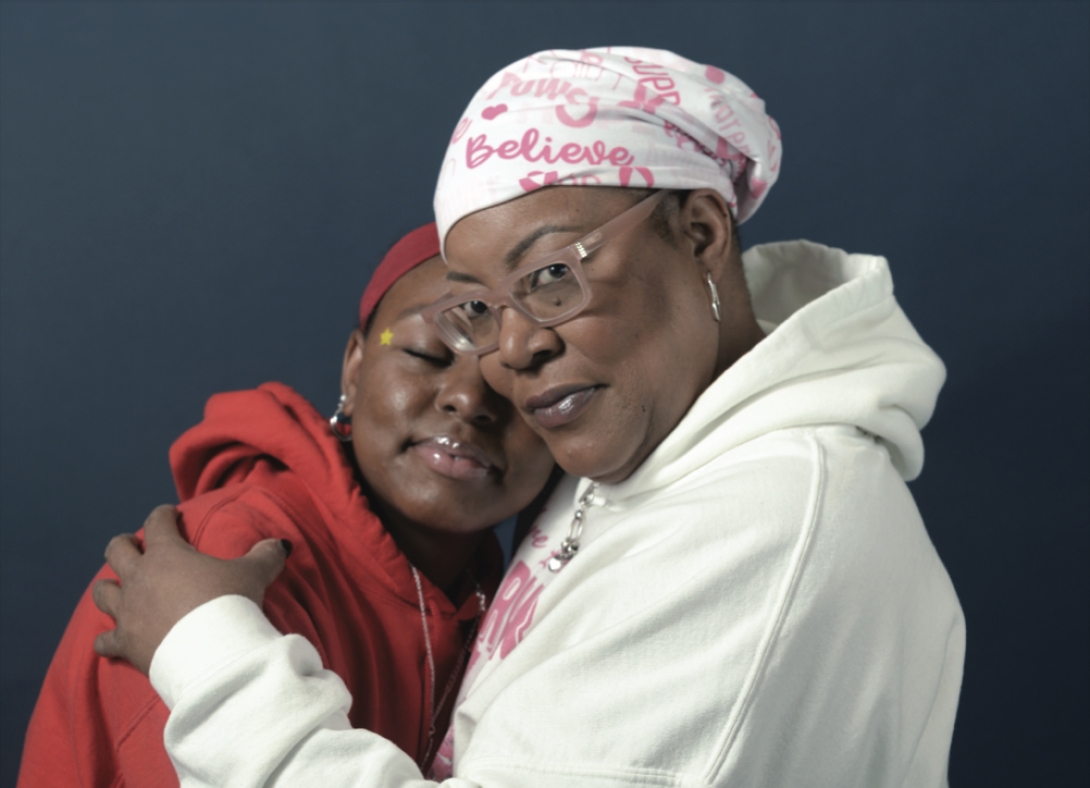 Portrait of Shantell and her daughter. Shantell is wearing a white sweatshirt and white headscarf. She's hugging her daughter who is wearing a red sweatshirt.