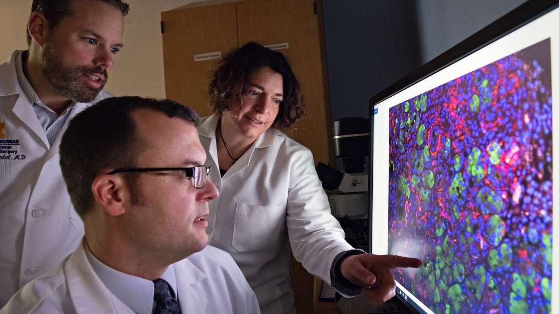 Three scientists lean in to examine a computer screen with a colorful image