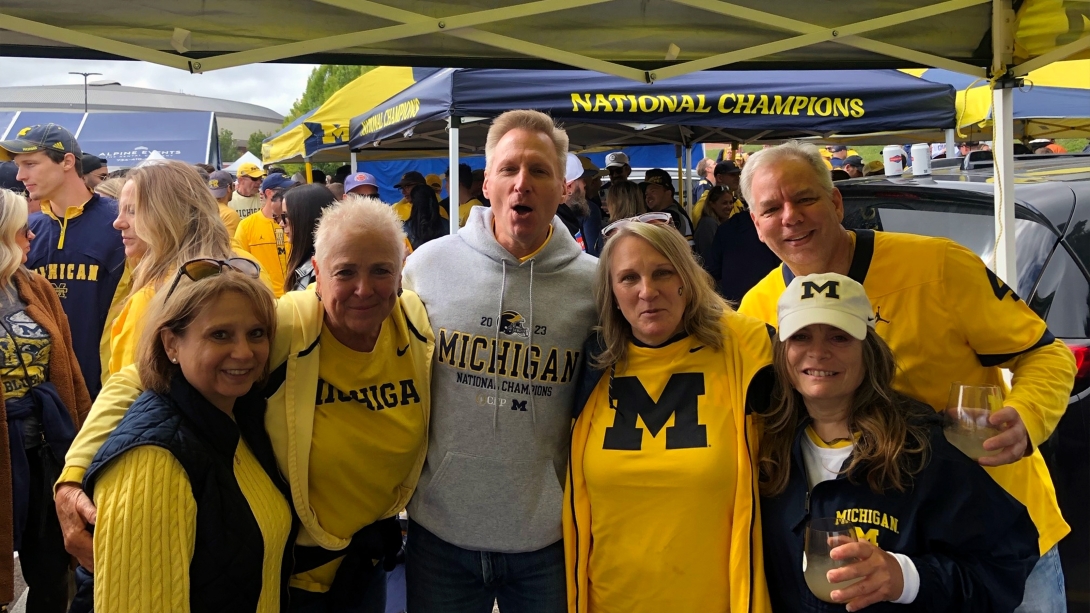 group of friends in UM gear at football game smiling at camera