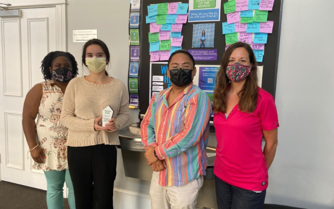 Small group of masked participants smile for photo in front of poster